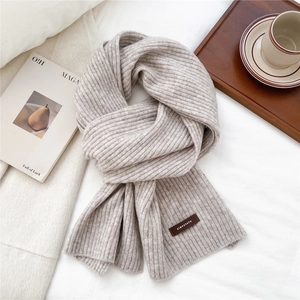 Detailed view of knitted scarf texture with premium brown leather logo patch on beige fabric