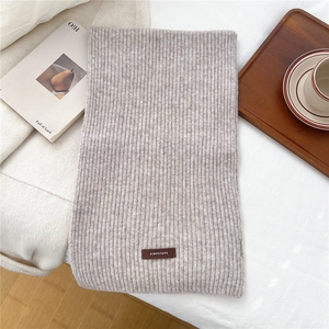 Detail view of oatmeal knit scarf with vertical stripes and premium faux leather brand tag