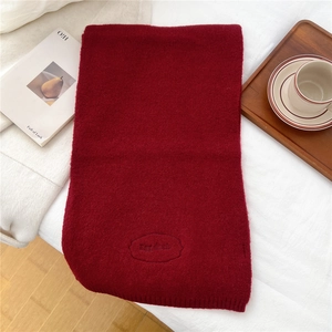 Detail shot of deep red knitted scarf showing dense wool texture and Egg dork embroidery