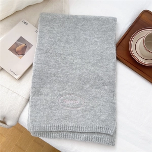 Close-up of gray knitted scarf featuring pink logo embroidery on a soft ribbed texture