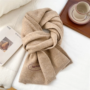 Close-up of beige knit scarf showing soft texture and red embroidered Egg doris logo