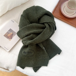 Close-up of dark green knitted scarf showing rich texture and embroidered logo detail