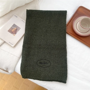Close-up of moss green thick knit scarf with Egg Doris logo embroidery on textured fabric