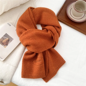 Detailed macro view of burnt orange knit scarf with embroidered logo and ribbed edges