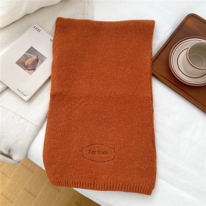 Detail of caramel knitted scarf featuring an embroidered Egg Doris logo and ribbed edges