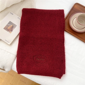 Detail of deep red knitted scarf featuring a delicate embroidered oval brand logo