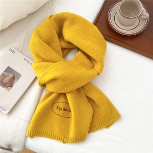 Detailed close-up of bright yellow knitted scarf with premium embroidered logo patch