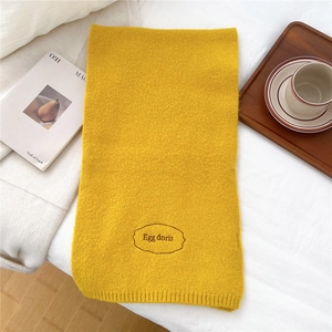 Close-up of yellow knitted scarf with Egg doris embroidery on soft white bedding background