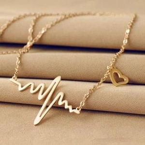Detail of gold heart monitor wave pendant with small side heart on beige fabric texture