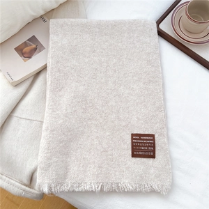 Dettaglio di sciarpa in maglia beige con frange ed etichetta su tessuto bianco morbido