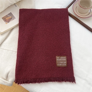 Dettaglio della sciarpa in maglia bordeaux con etichetta in lana e lunghe frange