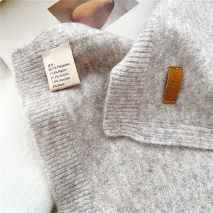 Detail of oatmeal knit scarf showing soft blend texture and premium leather logo tag