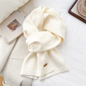 Detailed texture of cream knit scarf featuring a classic brown leather logo patch