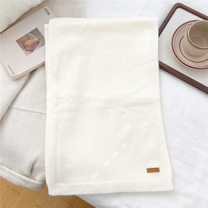 Close-up of white knit scarf texture with a brown leather patch and cozy lifestyle props