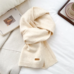 Detail of cream knit scarf showing fine texture and brown embossed leather logo label