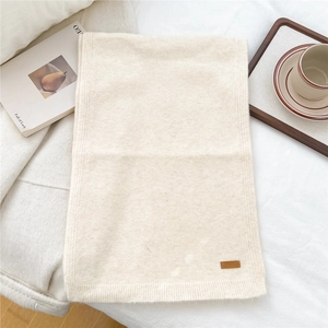 Detail of soft cream knitted scarf with brown leather patch and ribbed edge texture