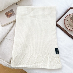 Detail of white knit scarf featuring diamond pattern texture and small brand woven label