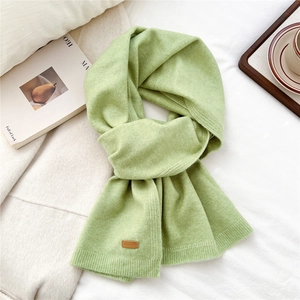 Detail of light green knit scarf featuring a brown leather label on soft fabric