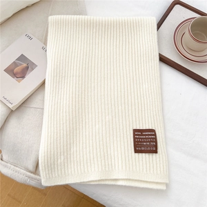 Macro shot of warm white knitted scarf with thick rib texture and brown woven label