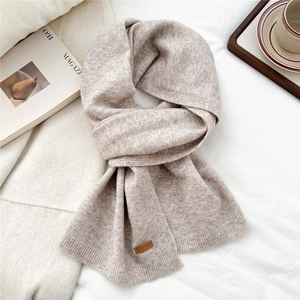 Close-up of oatmeal knit scarf texture with a brown leather label on a white background