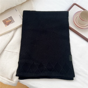 Detail of black knit scarf featuring diamond pattern texture and woven side label