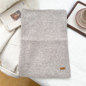 Close-up of soft knit scarf with textured ribbing and decorative brown leather label