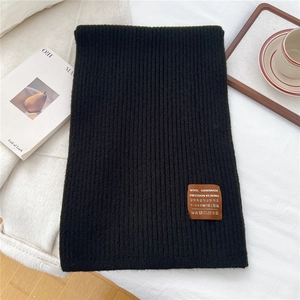 Detail of dark green knit wool scarf featuring a vintage leather handmade brand label