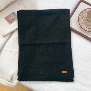 Detail of dark green knit scarf featuring a premium brown leather label on soft fabric