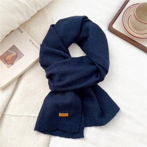 Detailed view of dark blue knitted scarf featuring a brown leather patch on soft wool texture