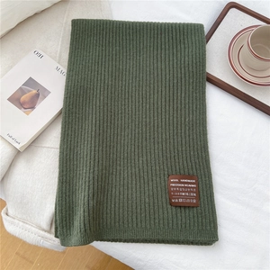 Close-up of dark green ribbed wool scarf featuring a handmade brown leather label detail