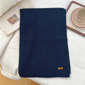 Detailed view of the navy blue knitted scarf texture with a brown leather logo patch