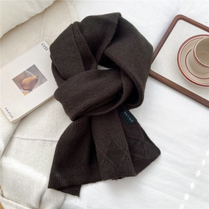 Macro view of dark coffee knitted scarf featuring diamond pattern and brand woven label