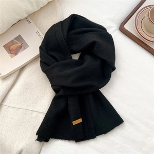 Detailed texture of black knit scarf featuring a brown leather label on a cozy background