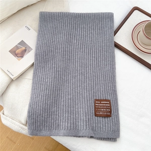 Close-up of gray rib-knit scarf texture with brown leather patch detail on white fabric