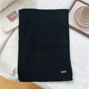 Detail of black knit scarf featuring thick wool texture and a premium brown leather tag