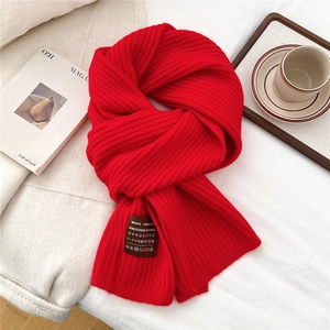 Detail of red ribbed knit wool scarf with handmade textile label on fabric surface