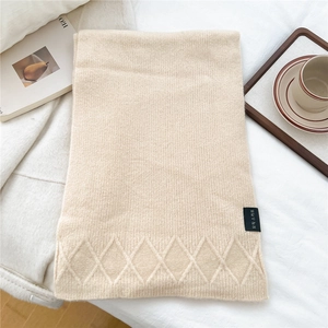 Detail of beige knit scarf with diamond pattern and brand label on white bedding