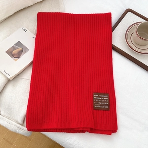 Close-up of red knitted scarf with vertical ribbed texture and brown woven fabric label