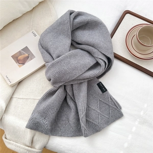 Close-up of light gray ribbed knit scarf with diamond pattern texture and woven label