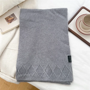 Close-up of gray knit scarf featuring classic diamond pattern and stitched black label