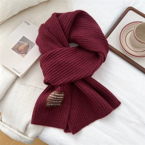 Close-up of thick rib-knit texture and handmade label on a warm wine red wool scarf