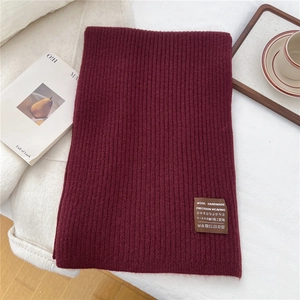 Macro detail of wine red ribbed knit scarf showing wool handmade tag and texture