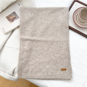 Detail of knit scarf texture with brown leather tag on beige fabric background