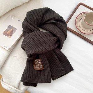 Close-up of dark brown ribbed knit scarf with hand-stitched label on soft fabric