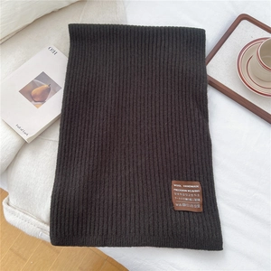 Detail of dark brown knitted scarf showing thick ribbed texture and wool handmade label