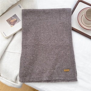 Close-up of dark coffee knit scarf texture with a brown leather logo patch on soft linen