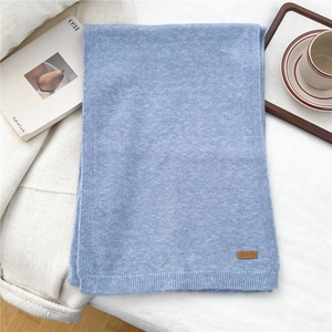 Detail of light blue knit scarf texture with a brown leather label on soft fabric