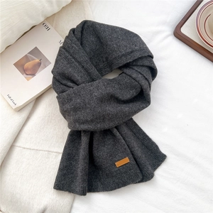 Detail of dark grey ribbed knit scarf featuring a brown square leather logo patch decoration