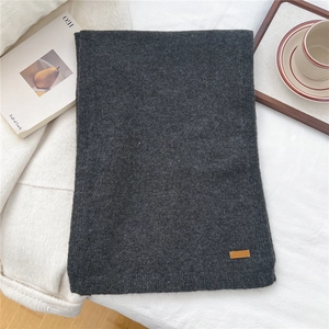 Detailed close-up of dark grey knitted scarf featuring a brown leather brand logo label