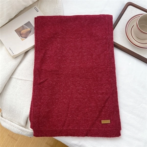 Detail shot of a dark red knitted scarf showing ribbed edges and a brown leather logo tag